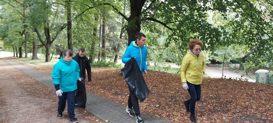 Grupa uczniów wraz z nauczycielem idzie przez park. Niosą worki na śmieci.