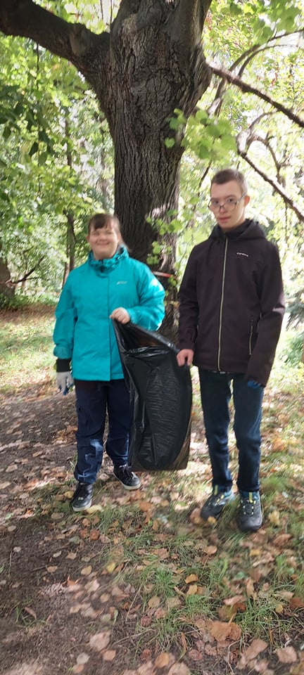 Dwoje uczniów stoi w parku z workiem na śmieci.